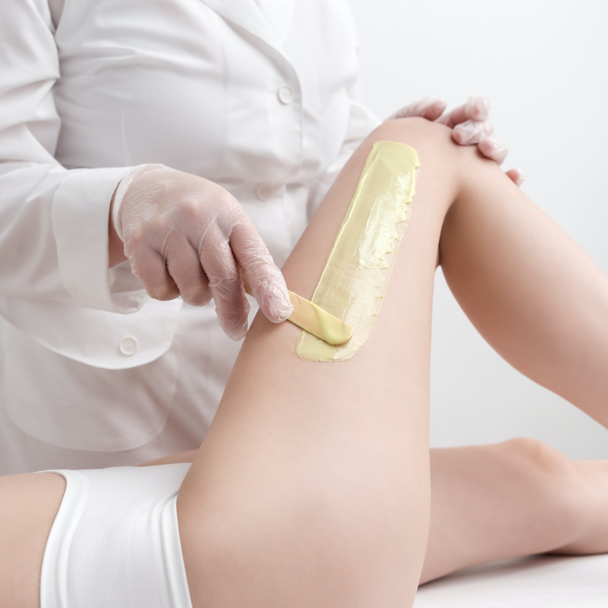 Waxing procedure - applying green hot wax on skin leg using spatula while woman lying down on couch